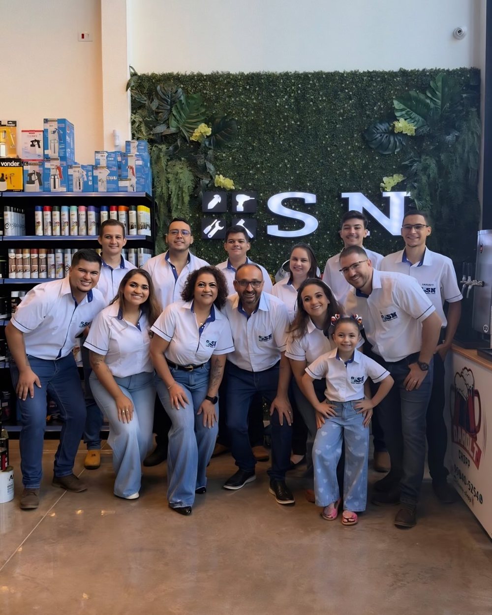 Equipe da SN Ferragens diante da parede verde com o logo, dentro da loja
