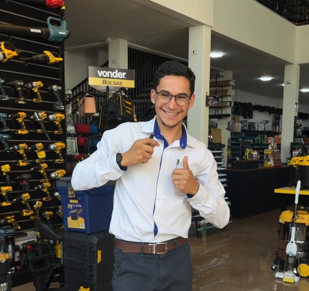 Atendente da SN Ferragens ao lado da parede de ferramentas elétricas